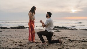 Une scène de plage où une personne est à genoux et fait une demande en mariage à une autre personne, qui est debout.