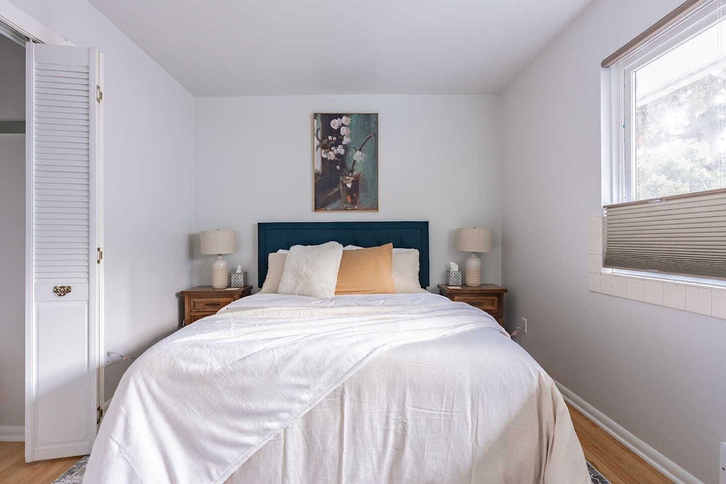A bedroom with a bed, two bedside tables, a painting, a window, and a door.