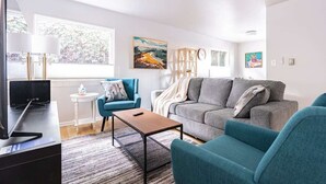 A modern living room with a grey sofa, teal armchairs, a coffee table, and a TV on a black stand.