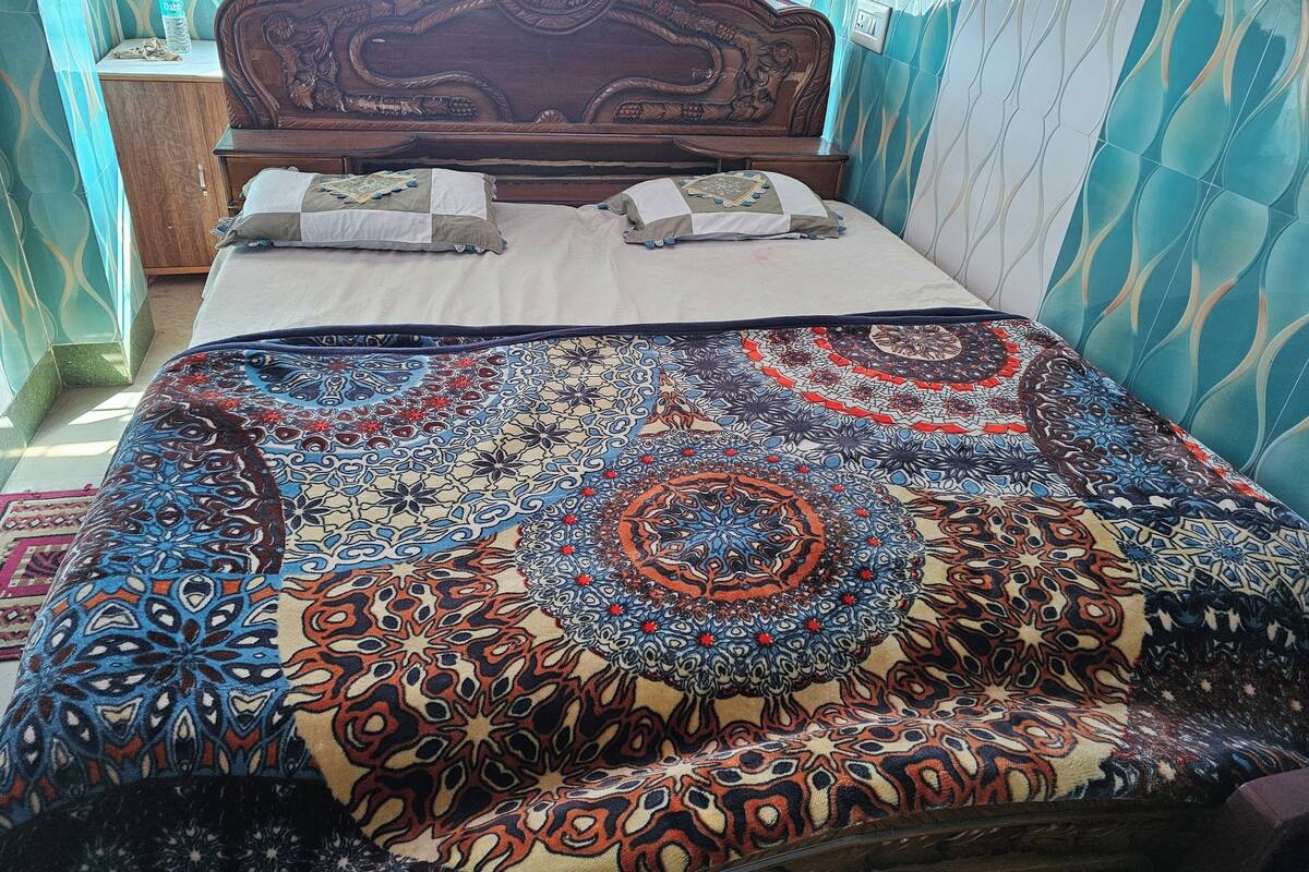 A bed with a patterned bedspread, a wooden headboard, and a nightstand with a bottle.