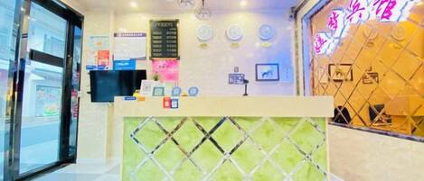 A hotel reception area with a reception desk, a digital screen, and a neon sign.