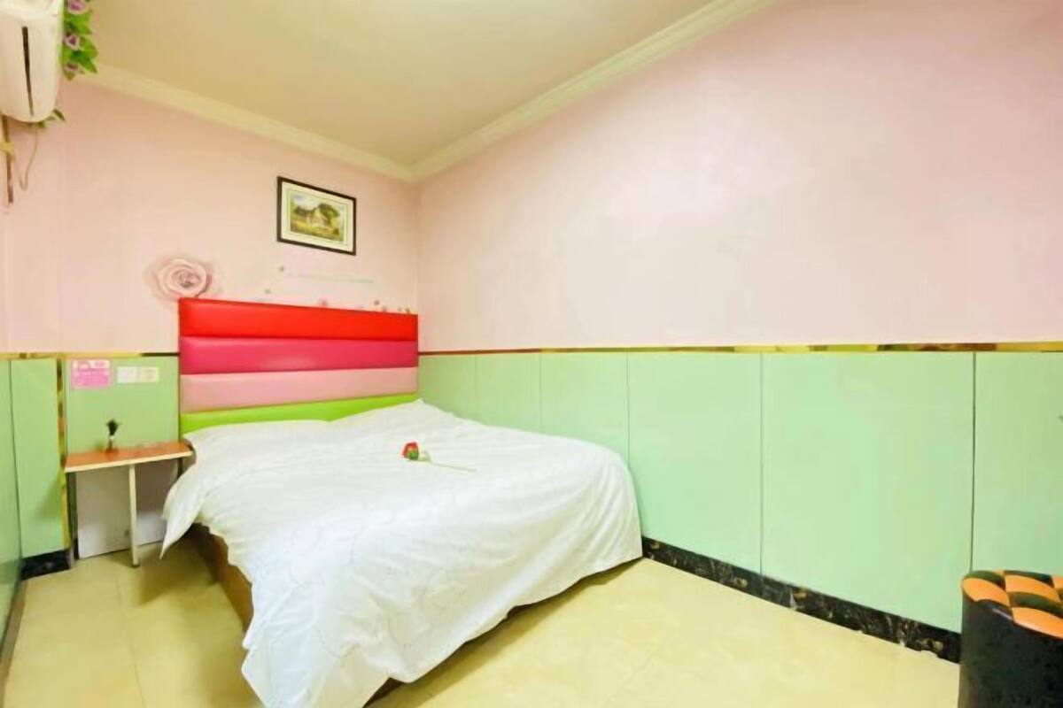 A bedroom with a bed, a nightstand, a wall-mounted air conditioner, and a small table.