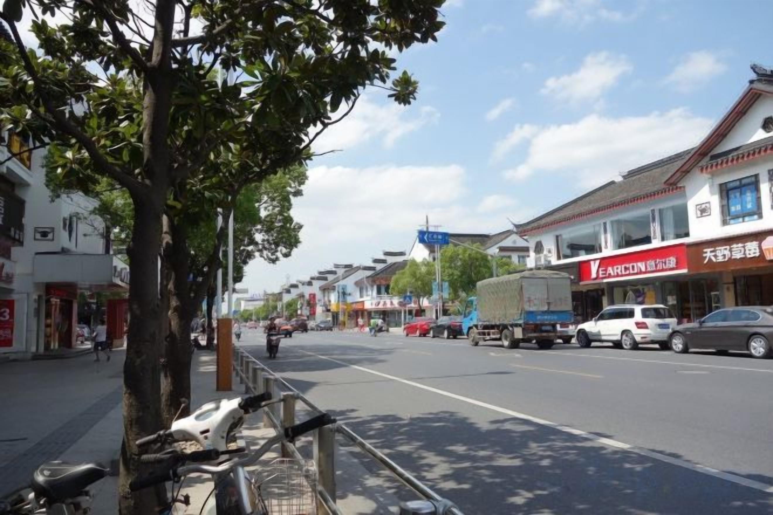 A street with shops, a tree, and parked vehicles.