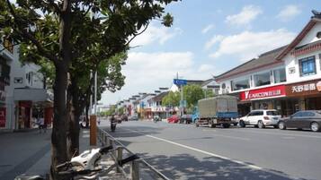 A street with shops, a tree, and parked vehicles.
