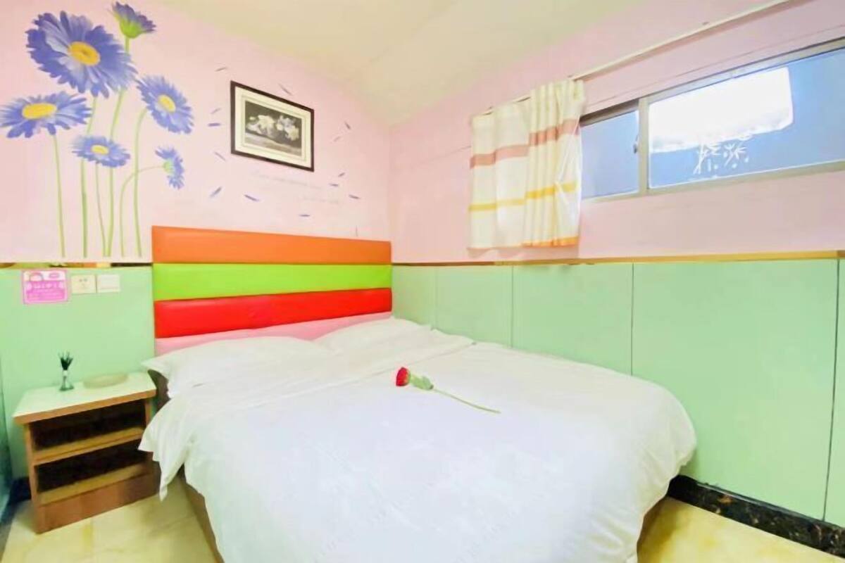 A bedroom with a bed, a nightstand, a window with curtains, and a wall with a floral mural.