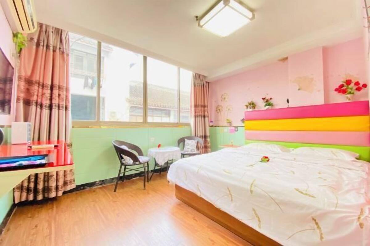 A bedroom with a bed, a desk, a chair, a small table, and a window.