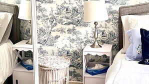 Een slaapkamer met een bed, nachtkastjes, een lamp, een spiegel en een rieten mand.