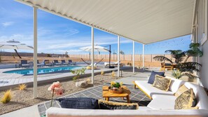 A covered outdoor area with a pool, lounge chairs, and a seating area with a table and cushions.