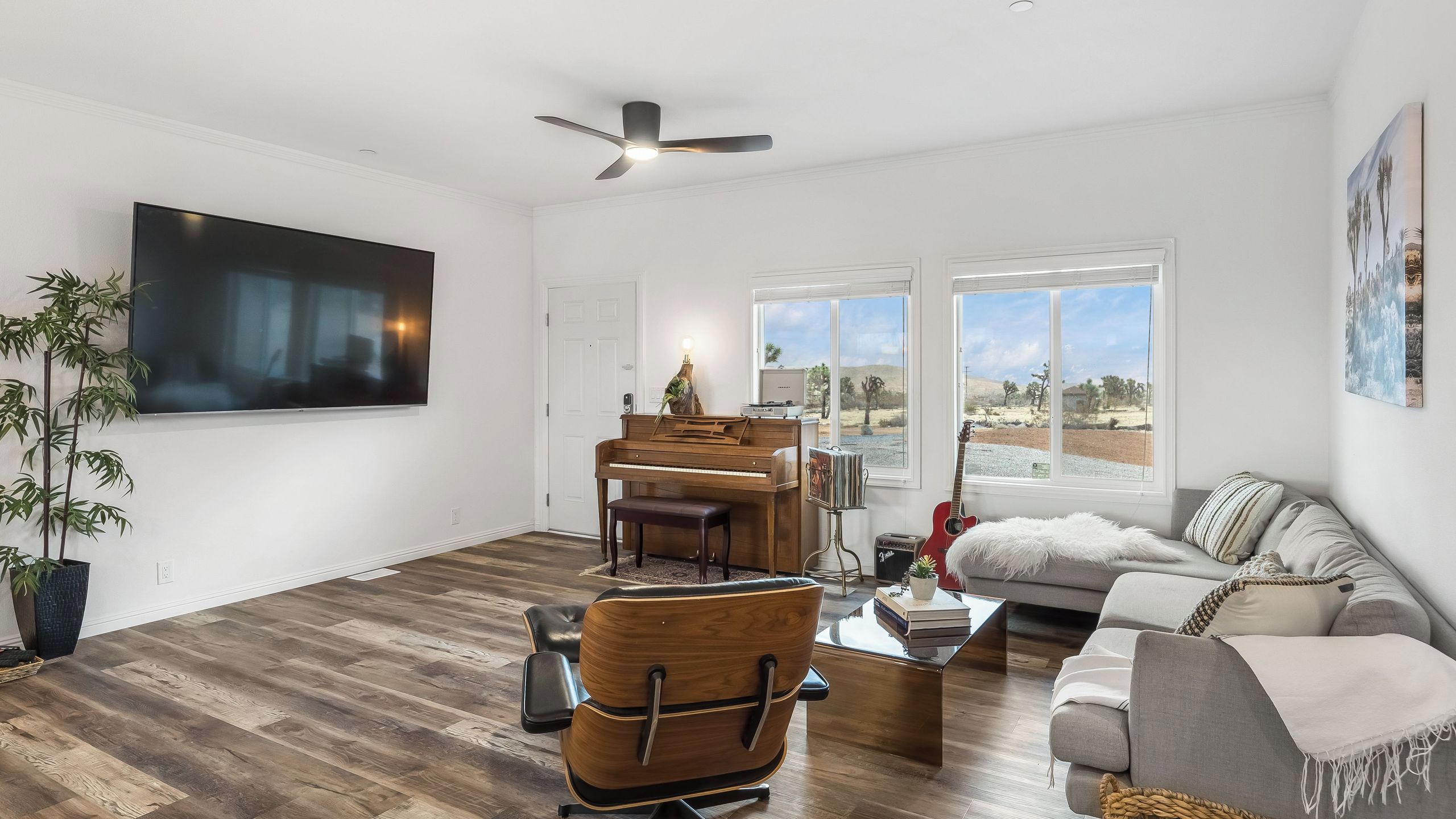 A spacious living room with a large flat-screen TV, a piano, a sofa, and a ceiling fan.