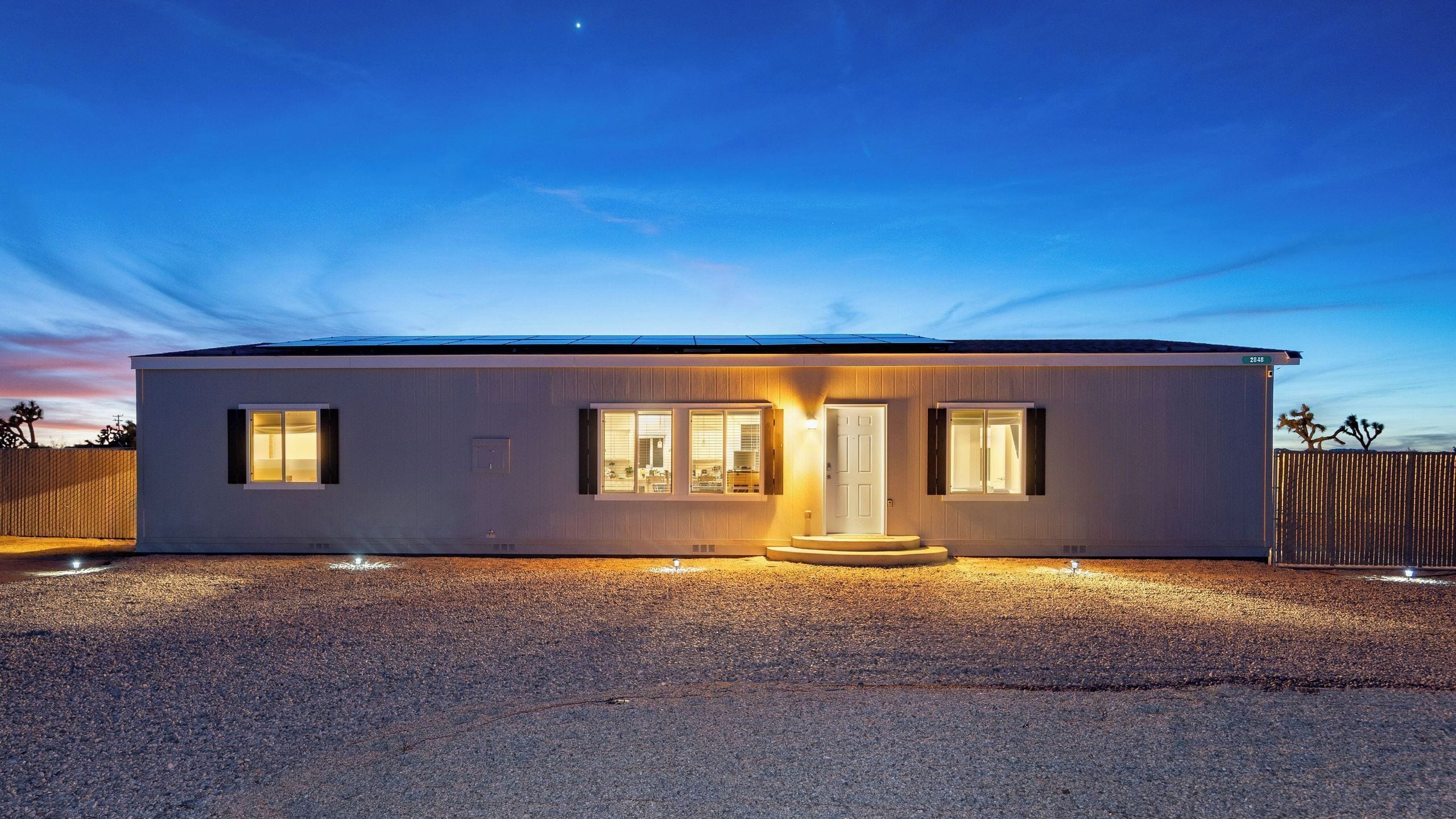 A modern single-story house with a flat roof, a front porch, and a gravel driveway.