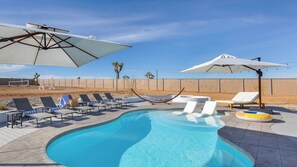 A swimming pool with lounge chairs and umbrellas, surrounded by a fence and desert landscape. - Pool, Spa, Pickleball & Piano Near Pioneertown Harmony House by Avantstay (Yucca Valley)