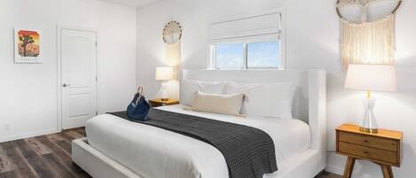 A bedroom with a large bed, a nightstand, a wall-mounted macrame piece, and a ceiling fan.