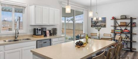 A modern kitchen with white cabinetry, a central island, and a dining area with wooden chairs.