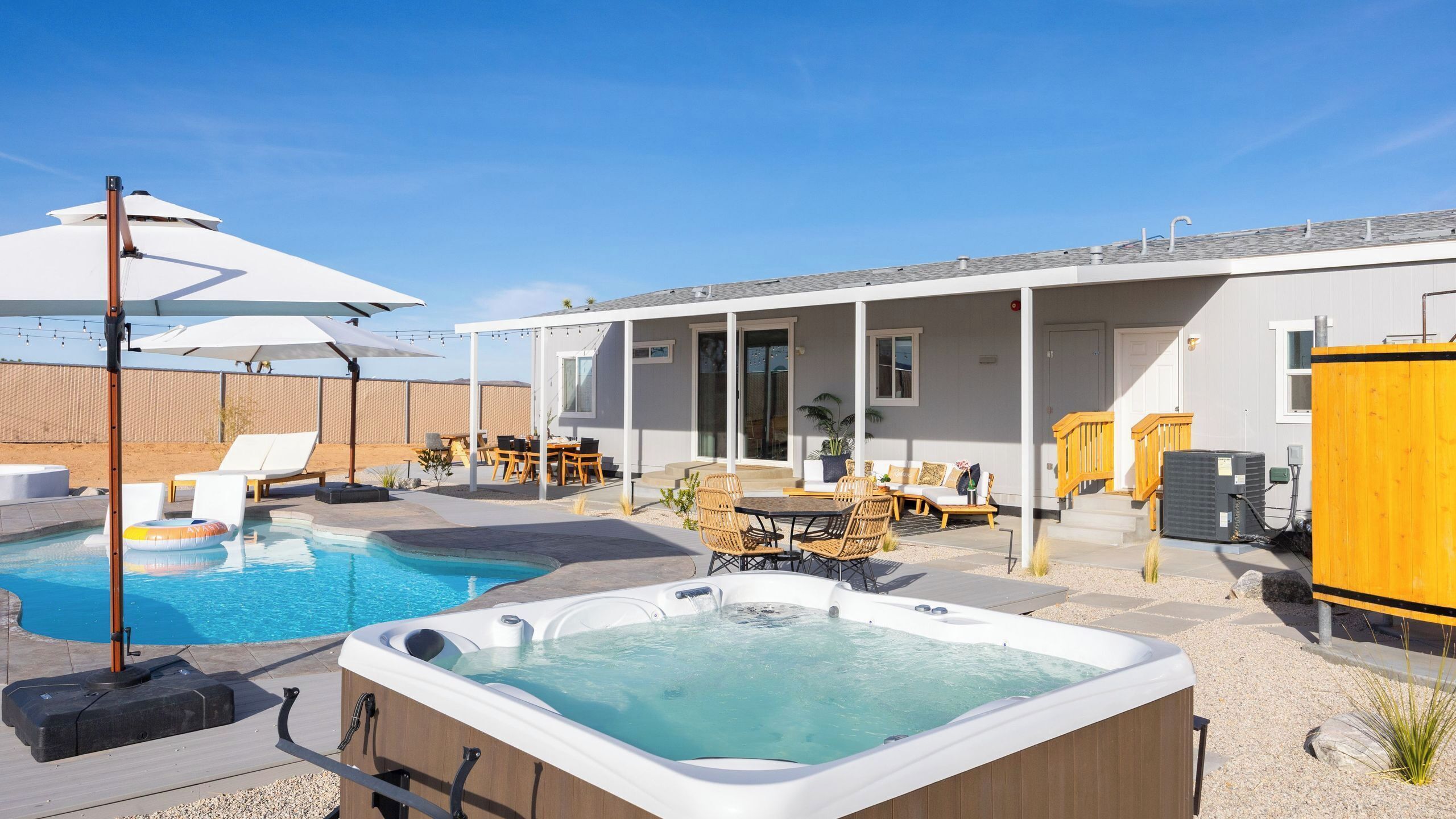 A pool area with a hot tub, lounge chairs, and a covered patio.