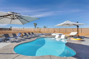 A swimming pool with lounge chairs and umbrellas, surrounded by a fence and desert landscape. - Pool, Spa, Pickleball & Piano Near Pioneertown Harmony House by Avantstay (Yucca Valley)