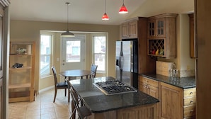 A kitchen with wooden cabinets, a black countertop, a stainless steel refrigerator, and a gas stove. There is a dining table with chairs and a pendant light above it. - 2 story, private, quiet upscale neighborhood MINUTES FROM 4 MAJOR SKI RESORTS (West Jordan)