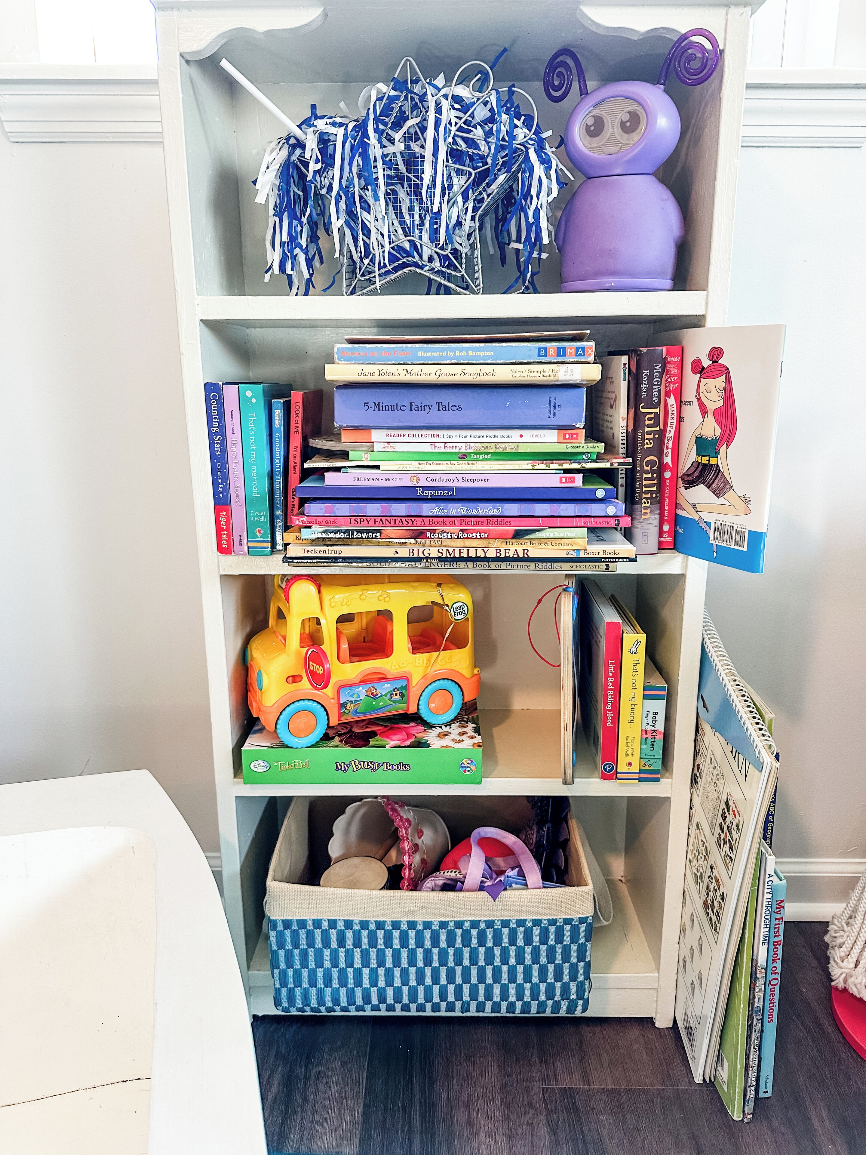 A bookshelf with various books, a toy bus, and a basket.