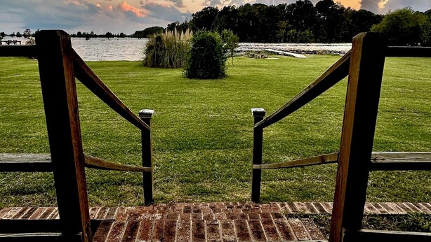 Gradi de fusta que condueix a una zona enjardinada amb vista a una massa d'aigua i arbres a la distància.
