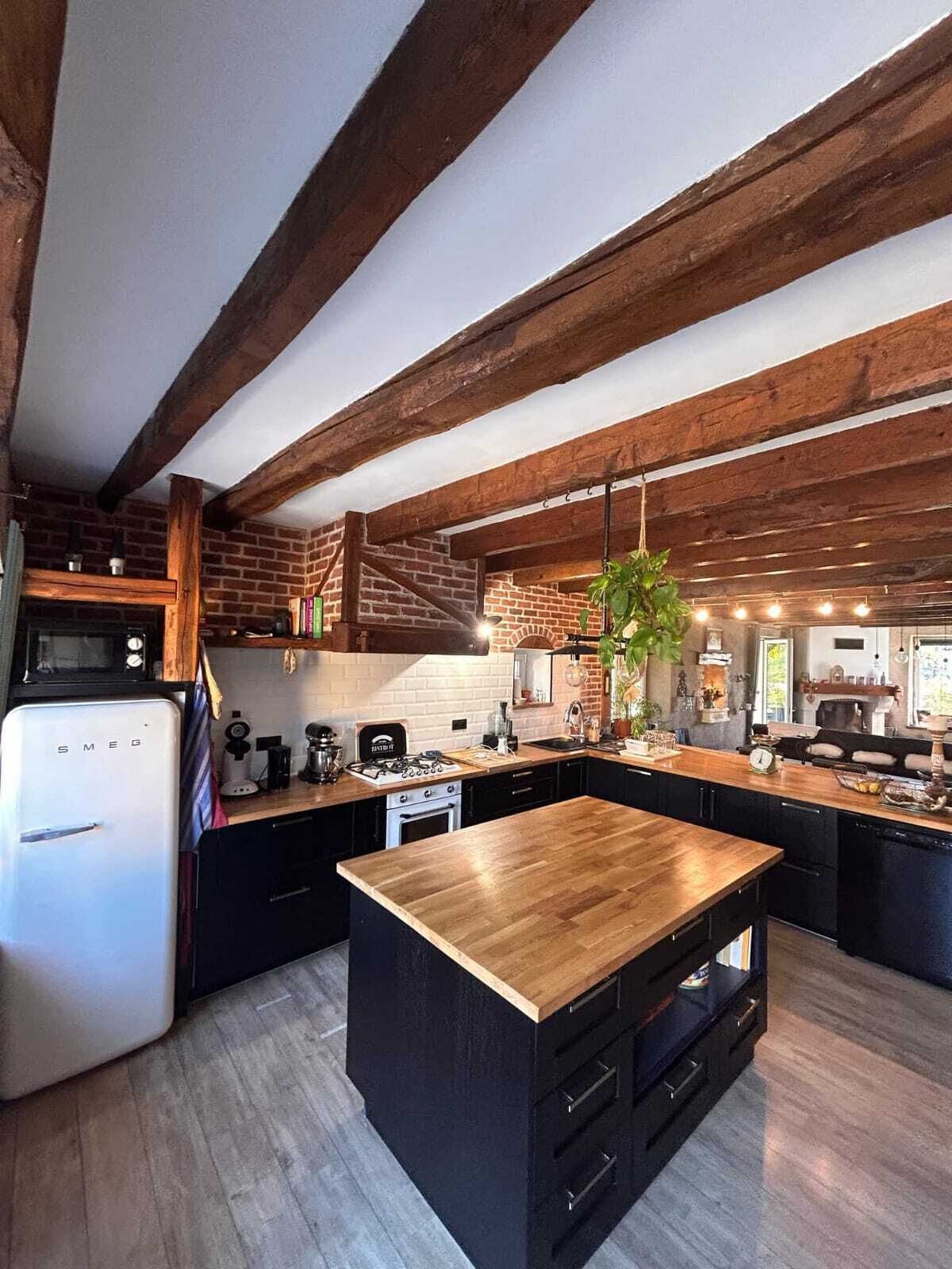 A modern kitchen with exposed wooden beams, a central island, and a built-in stove.