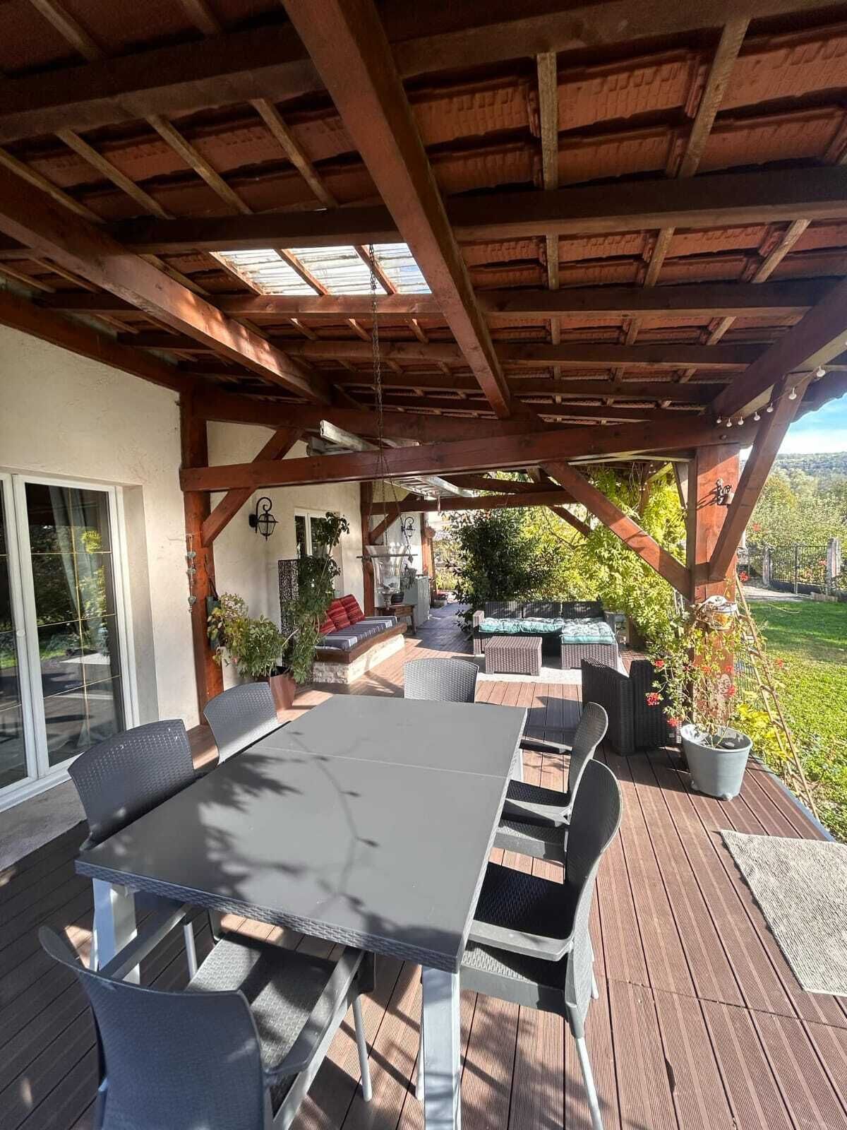 Un patio exterior con terraza de madera, una mesa con sillas y un área de estar cubierta con cojines y un brasero.