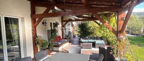 Un patio exterior con terraza de madera, una mesa con sillas y un área de estar cubierta con cojines y un brasero.