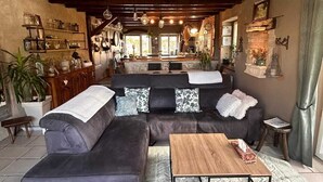 Uma sala de estar aconchegante com um sofá seccional, uma mesa de centro de madeira e uma cozinha ao fundo.