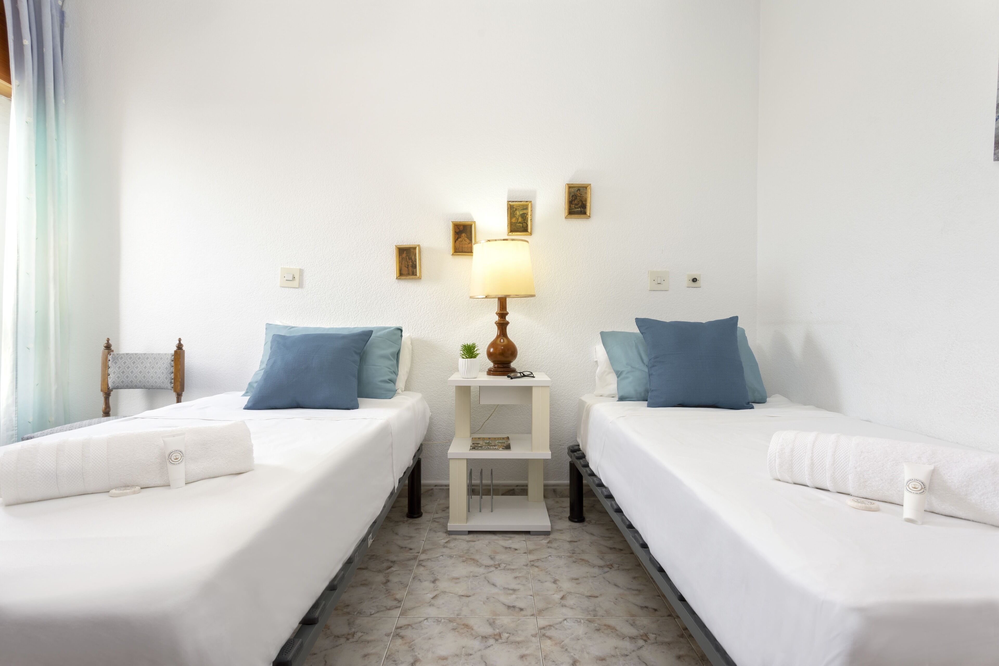 Ein Hotelzimmer mit zwei Betten, einem Nachttisch mit Lampe und einem kleinen Regal mit Dekoration.