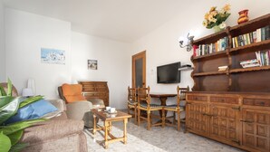 Een woonkamer met een bank, stoelen, een houten salontafel, een televisie en een boekenkast.