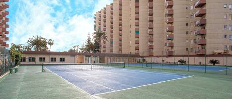 An outdoor tennis court surrounded by high-rise buildings.