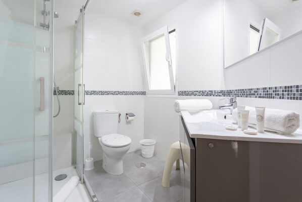 A modern bathroom with a glass shower enclosure, a toilet, a sink with toiletries, and a mirror. - Las Gondolas (Almunecar)