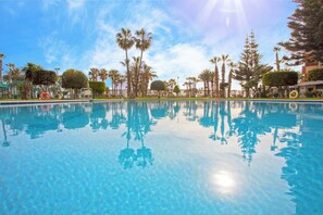 A clear blue pool surrounded by palm trees and a fence. - Las Gondolas (Almunecar)