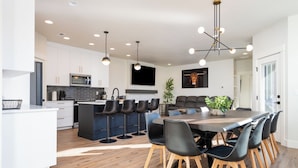 Une cuisine moderne avec des meubles blancs, un îlot central et un coin repas comprenant une grande table et des chaises.