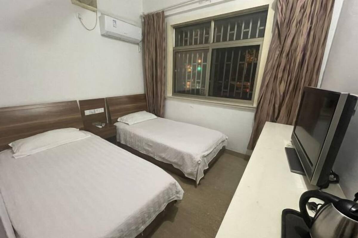 Habitación de hotel con dos camas individuales, un escritorio con televisor y una ventana con rejas.