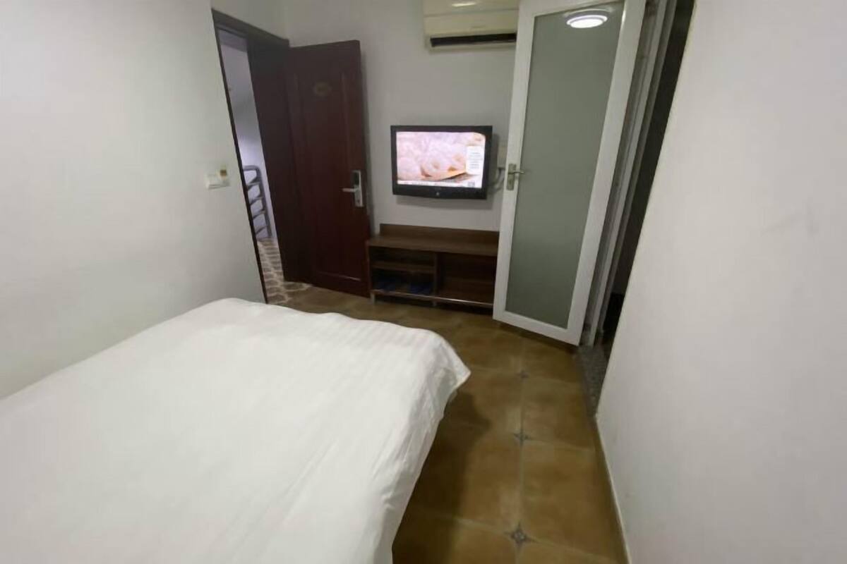 Un dormitorio con una cama, un televisor en la pared y una puerta que da a otra habitación.