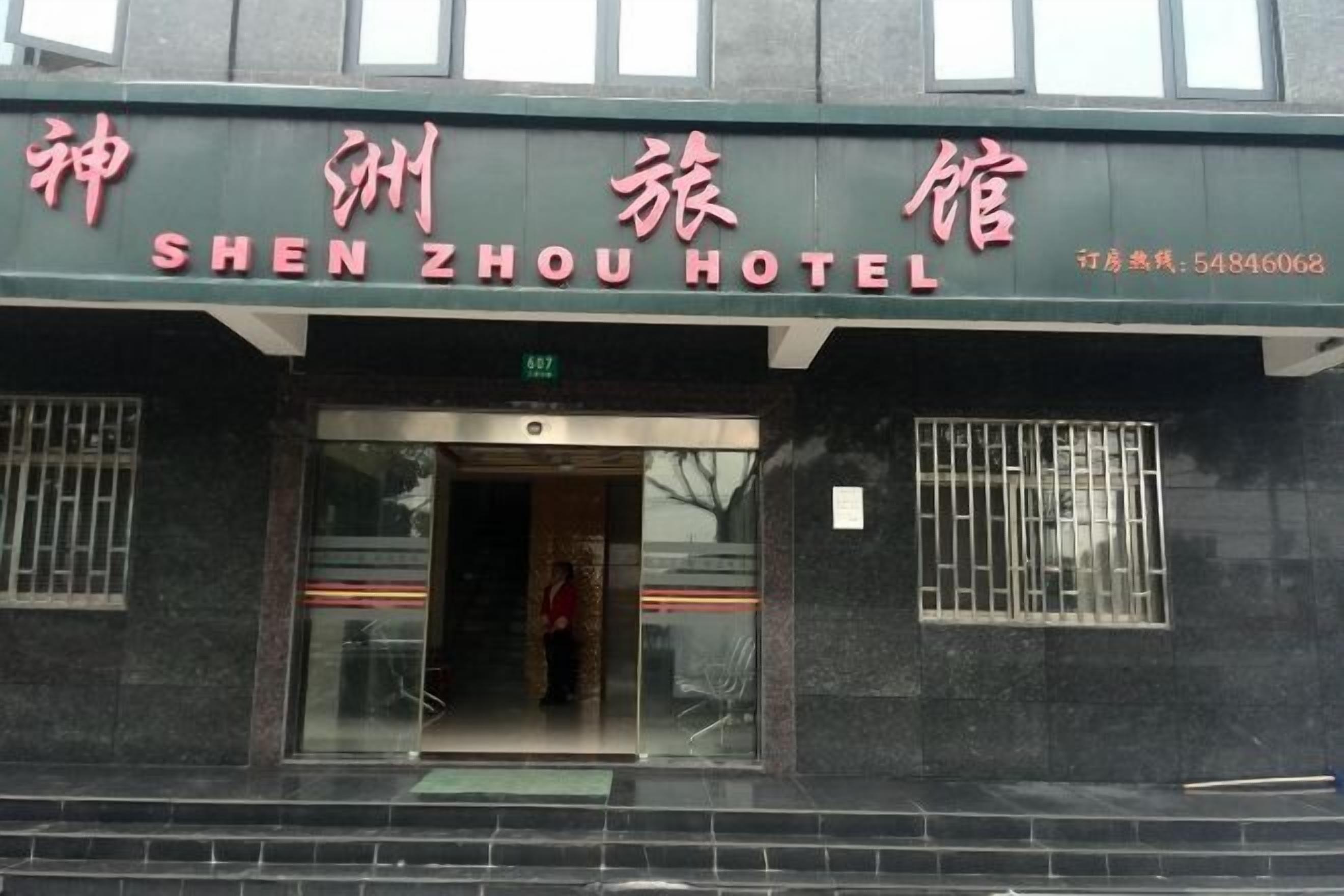 The exterior of the SHEN ZHOU HOTEL with a green facade and a glass entrance.