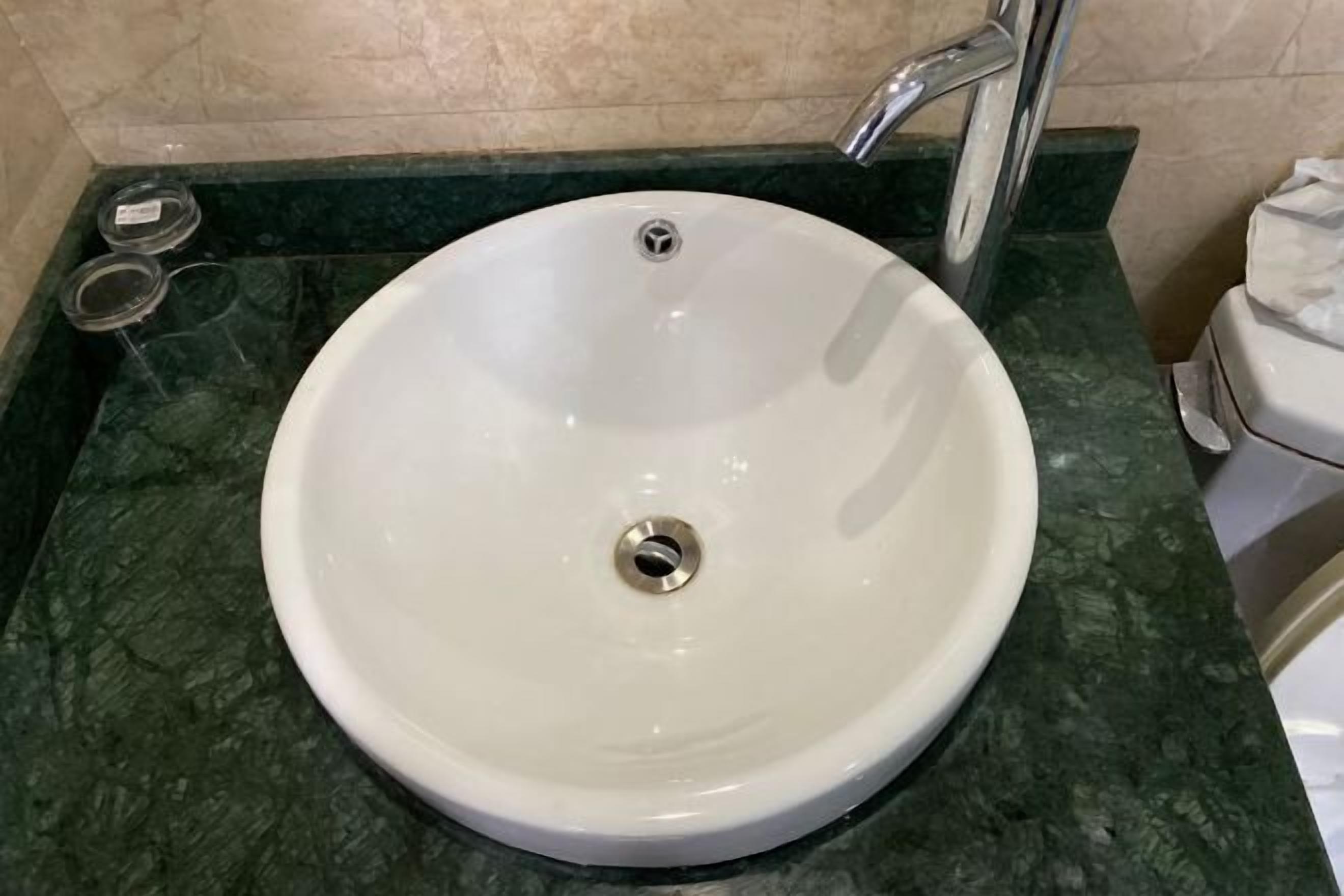 Un lavandino bianco con un solo scarico, posato su un piano di marmo verde in un bagno.