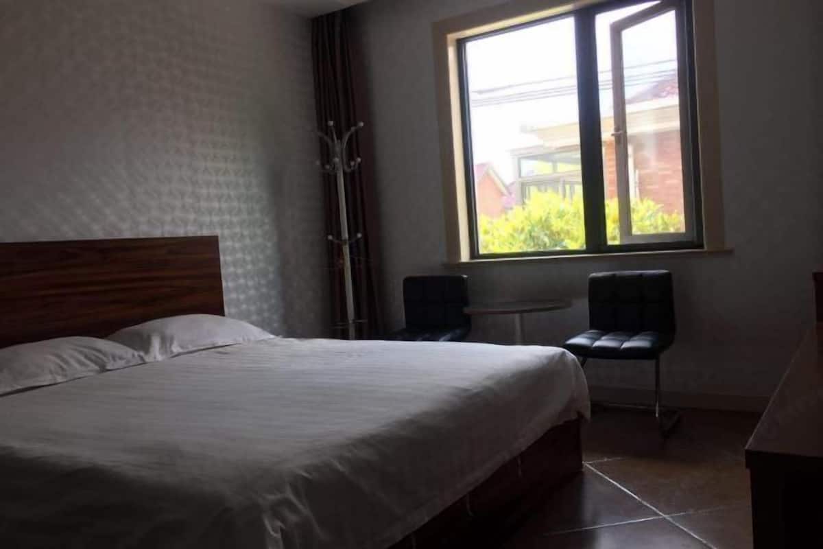 Un dormitorio con cama, ventana, una silla y una mesita.
