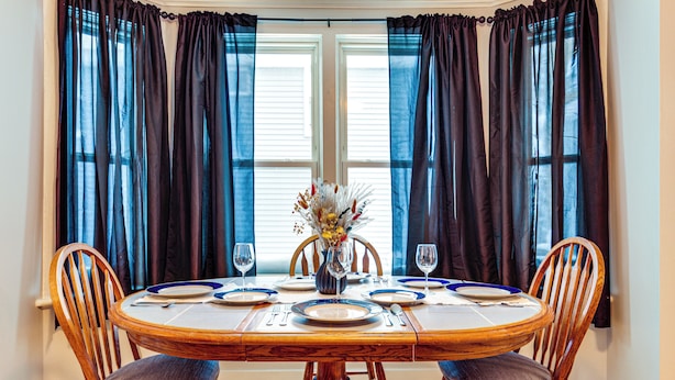 Een eettafel gedekt voor vier personen, met stoelen, een vaas met bloemen en een raam met gordijnen.