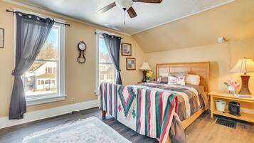 Une chambre à coucher avec un lit, un ventilateur de plafond, une table de chevet avec une lampe et une fenêtre avec des rideaux.
