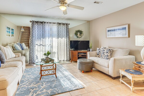 A living room with a sofa, ottoman, coffee table, TV, and a staircase. - Walk to Beach: PCB Gem w/ Community Pool Access! (Panama City Beach)