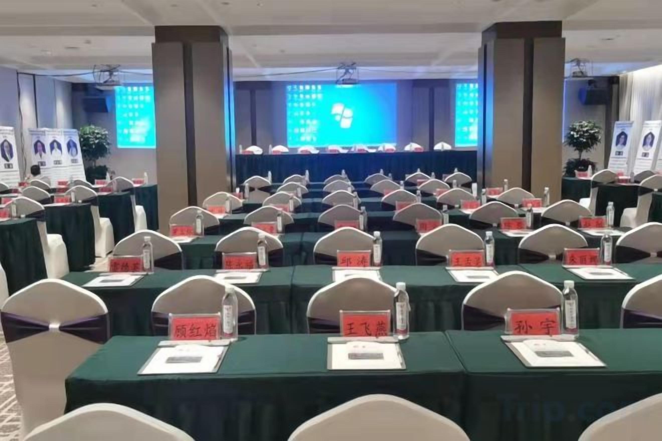 A conference room with rows of tables, name cards, and a presentation screen in the background.