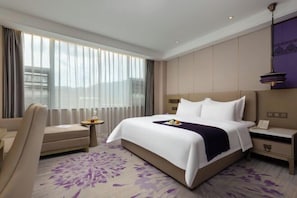 A hotel room with a large bed, a sofa, a small table with a fruit bowl, a nightstand, and a large window with curtains. - Yelang Hotel (Hezhang)