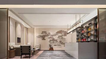 Um interior moderno com piso de mármore, área de estar com sofá e poltronas, parede decorativa com arte abstrata e estante com diversos objetos.