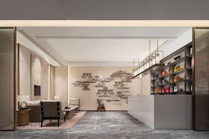 Un interior moderno con piso de mármol, una zona de estar con sofá y sillones, una pared decorativa con arte abstracto y un estante con diversos objetos.