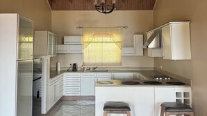 A modern kitchen with white cabinets, a central island with stools, a chandelier, and a window with a lace curtain. - 2BR Hip Strip•Ocean View Balcony•Steps to Beach (Montego Bay)