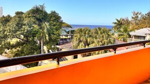 A balcony with a checkered floor, overlooking a coastal area with palm trees and a view of the ocean. - 2BR Hip Strip•Ocean View Balcony•Steps to Beach (Montego Bay)