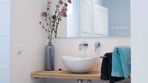 Een moderne badkamer met een wit wastafelmeubel, een spiegel en een vaas met bloemen.