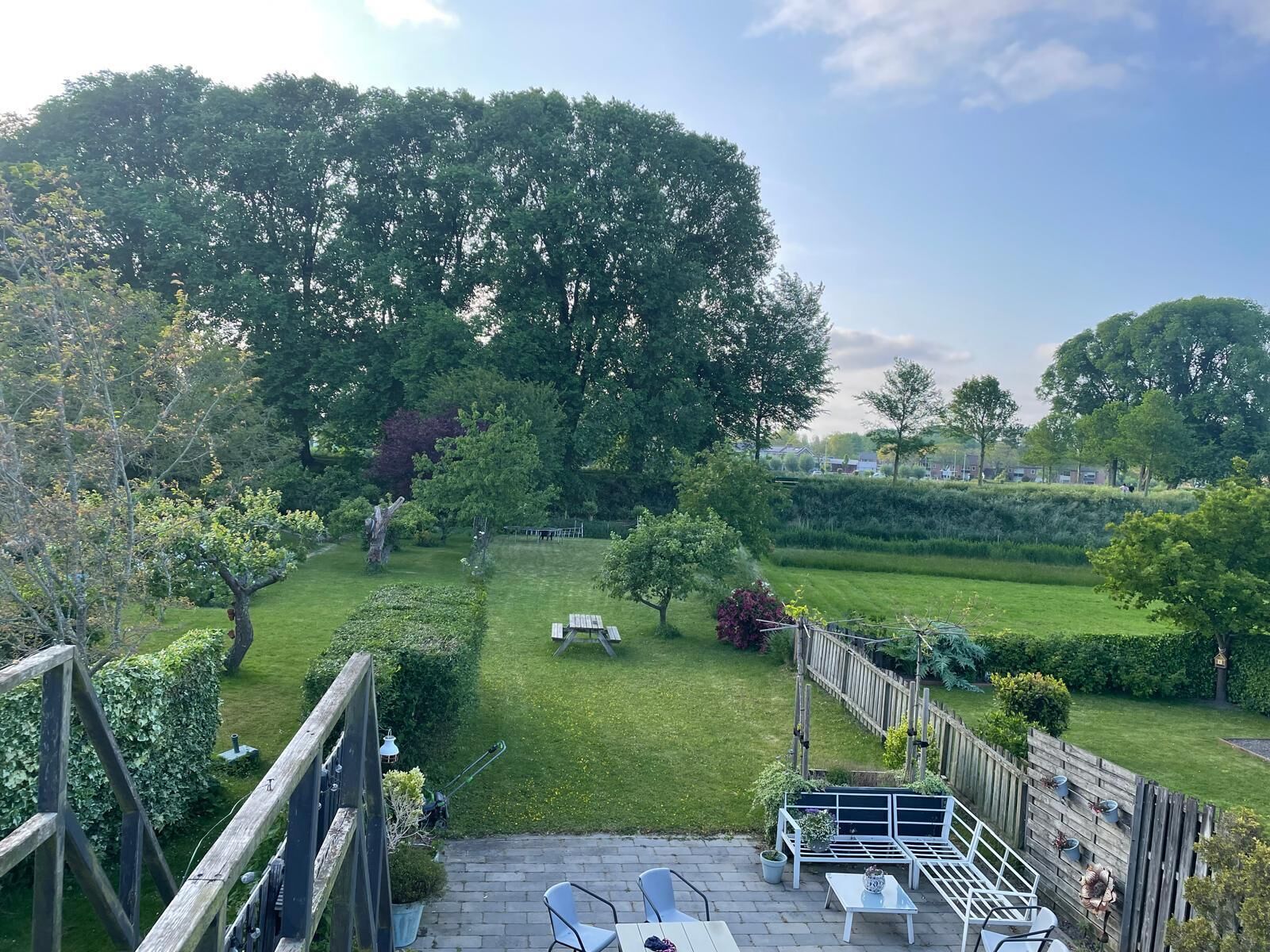 Uma área de pátio com deck de madeira, mobiliário para área externa e vista para um jardim e gramado bem cuidados.