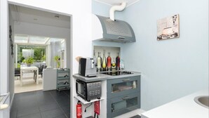 Een moderne keuken met een inbouwoven, magnetron en afzuigkap. Er is een eethoek zichtbaar door een open deur.