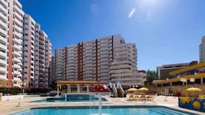 Una piscina con fontana centrale, circondata da lettini e ombrelloni, con edifici alti sullo sfondo.